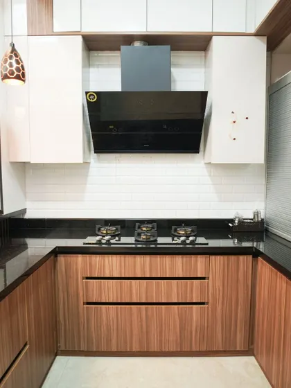 A close-up of the cooking area in a U-shaped kitchen, showing the rich texture of the wood-grain laminate on the lower cabinets. The design is complemented by a black chimney and white subway tile backsplash.