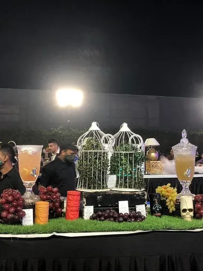 A rustic-themed mocktail bar on a grass-covered table, featuring fresh fruit juices, decorative birdcages, and unique glassware.