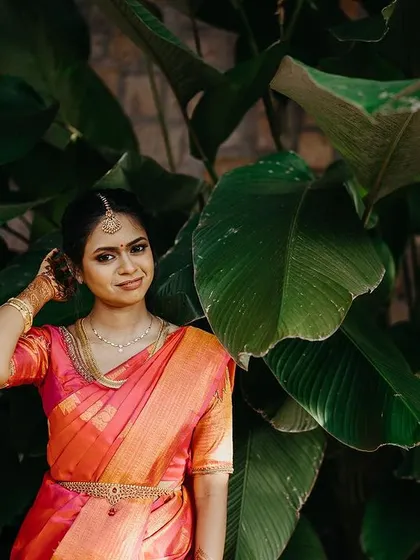 A beautiful portrait of a South Indian bride, her vibrant saree framed by lush greenery.