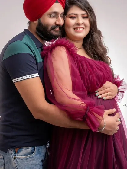 A gentle and loving pose from a studio maternity session. The husband embraces his wife from behind, both with happy smiles, creating a warm and intimate portrait.