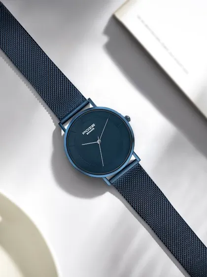 Styling a deep blue Sonata watch for a morning-themed shot. The composition includes a coffee cup and an open book, creating a relaxed and aspirational mood that integrates the product into a daily routine.