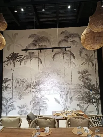A monochrome tropical jungle mural sets a sophisticated and modern tone in this restaurant. The black and white design is timeless and pairs beautifully with the natural textures of the wicker lighting and wooden furniture.