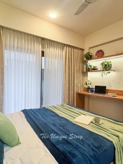 This bedroom includes a well-lit, built-in study desk with floating shelves. The combination of warm wood and white cabinetry creates a clean and inspiring workspace, complemented by natural light from the adjacent balcony.