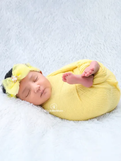 A splash of sunshine. This baby is wrapped in a bright yellow swaddle, curled up on a fluffy white blanket in a classic newborn pose.