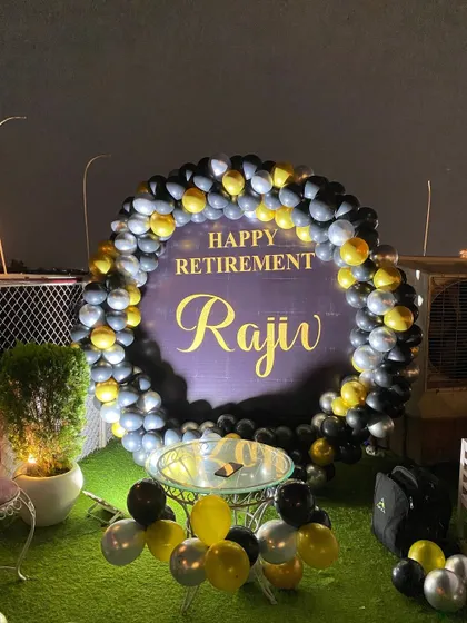 A sophisticated rooftop decoration for a retirement party. The circular balloon arch in black, silver, and yellow frames a custom 'Happy Retirement' sign.