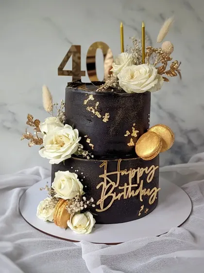 A striking black and gold two-tier cake for a 40th birthday. I used a rich black ganache and decorated it with white roses, gold macarons, and gold leaf for a dramatic and luxurious feel.
