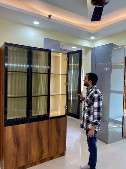 Here I am inspecting a newly installed crockery unit. This design features fluted glass doors with a black metal frame, set against a rich wood-finish cabinet.