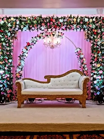 This reception stage at Jashan Banquet hall features three floral arches over a soft pink curtain backdrop. The design provides a wide, elegant space perfect for the couple and their families on stage.
