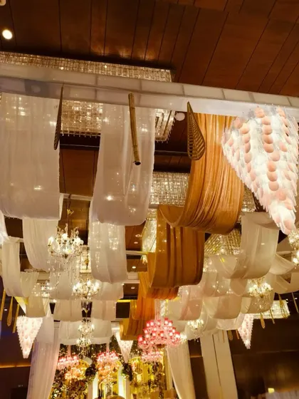A masterpiece of a ceiling, where flowing white and golden drapes meet shimmering chandeliers and delicate hanging elements, radiating warmth and luxury.