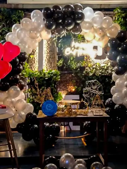 A sophisticated black, white, and silver balloon arch for a party in a cafe with a brick and ivy wall. The addition of red heart-shaped balloons adds a pop of color to this elegant and modern decoration.