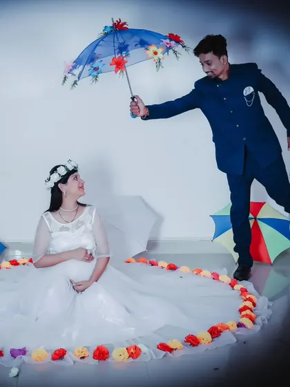 A creative studio maternity shoot, with the couple posing with colorful umbrellas and flower petals.
