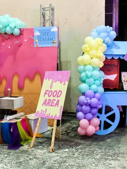 The food area at a Candyland party, featuring an ice cream station and a popcorn cart under a colorful balloon arch.