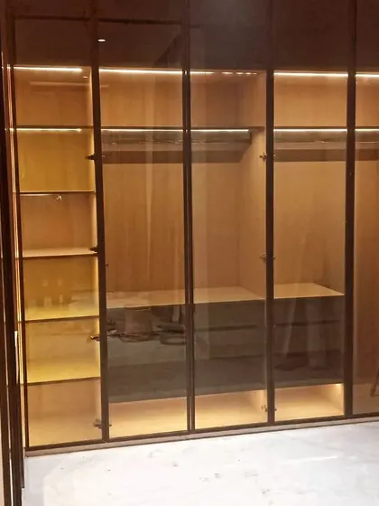 An open view of a walk-in wardrobe during installation. You can see the internal configuration with hanging rods, shelving, and a chest of drawers, all illuminated by profile lighting.