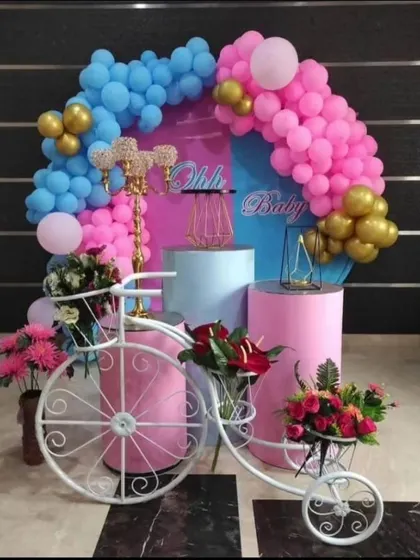 A sweet and simple baby shower setup with a pink and blue theme. The decorative bicycle filled with flowers adds a unique and charming touch.