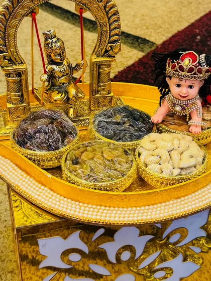 A closer look at a dry fruit platter for a naming ceremony. The golden tray is decorated with pearl details and features a baby Krishna doll, adding a divine touch.