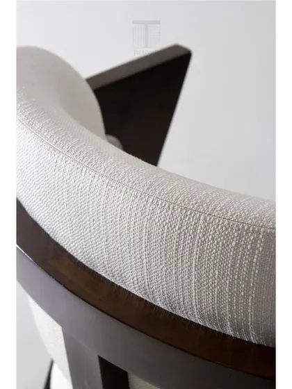 The curved backrest of this armchair is designed for ergonomic comfort, while the textured white fabric adds a touch of softness to the wooden frame.