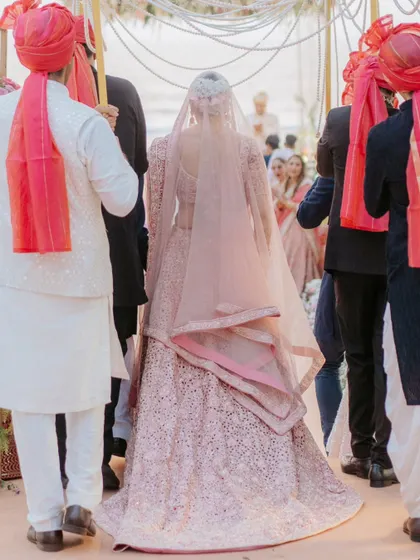 The bride's grand entrance. This shot captures the back of her stunning pink lehenga as she walks down the aisle, building anticipation for the groom.