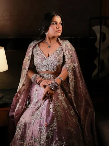A regal and dramatic look for a wedding reception. The makeup features deep, smokey eyes and a contoured face, perfectly complementing the heavily embroidered lavender lehenga and cape.