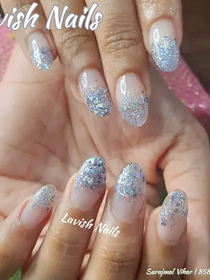 A dramatic glitter application with chunky silver glitter concentrated at the tips, fading into a clear base on natural-length nails.