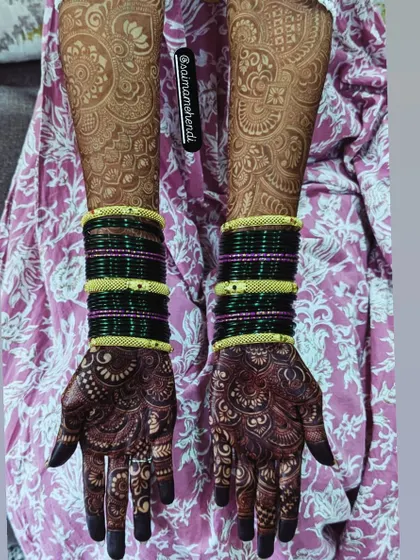A beautiful contrast between the dark stain on the hands and the lighter, faded pattern on the arms, paired with traditional green bangles.