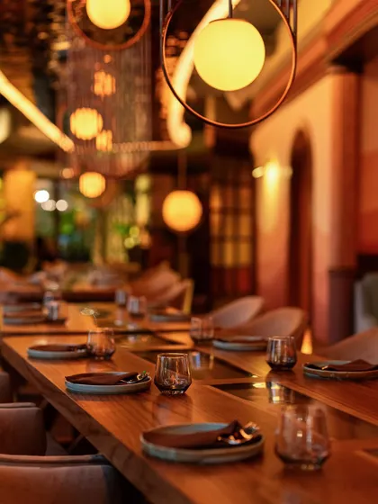 A close-up of our long dining tables, set and ready for guests. The warm, spherical pendant lights create an intimate and modern feel.