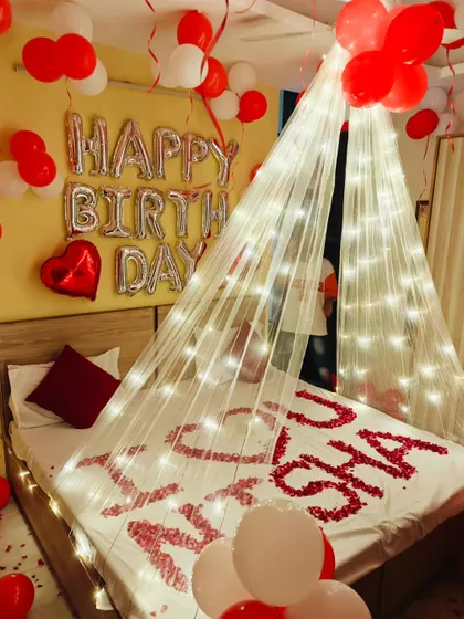 A romantic birthday surprise for a loved one. The bed is decorated with a fairy light canopy and their name spelled out in rose petals.
