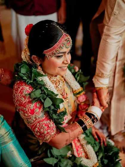A candid moment from the wedding ceremony. The bride's red blouse is heavily embroidered with traditional motifs, creating a stunning contrast against her light-colored saree.