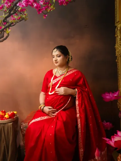 A moment of quiet reflection. Seated amidst lotus flowers and cherry blossoms, this expecting mother cradles her belly in a serene and artistic composition.