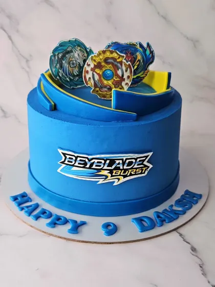 A Beyblade Burst cake for Daksh's 9th birthday. This vibrant blue cake is decorated with the iconic Beyblade logo and toy toppers for a true fan.