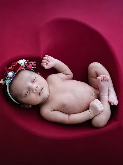 A baby in a natural, curled-up fetal position inside a heart-shaped posing bowl, creating a beautiful and symbolic image.