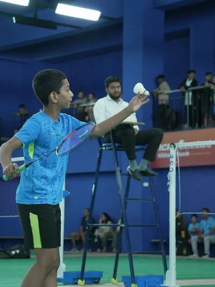 A junior player serves under the watchful eye of the umpire and a gallery of spectators, replicating the pressure of a professional match.
