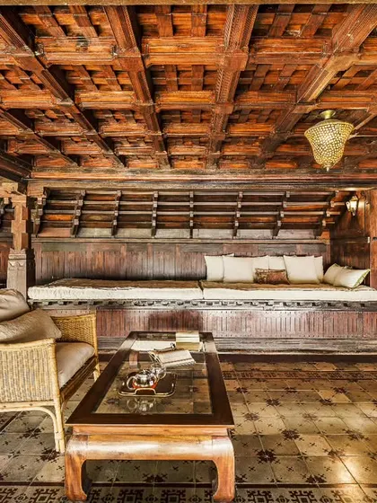 A cozy seating area within a heritage building, featuring intricate wooden ceilings and traditional furniture. Sunlight streams in, creating a warm and inviting space for relaxation.