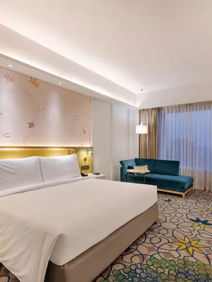 A spacious guest room designed for tranquility and comfort. The neutral color palette is accented by a custom carpet and a feature wall with graphic patterns that subtly reference Lucknow's cultural heritage.