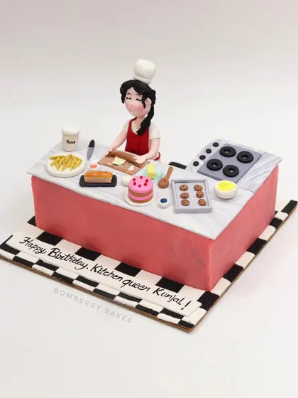 A cake for a "Kitchen Queen," featuring a detailed kitchen scene with a chef figurine, stove, and tiny edible baked goods.