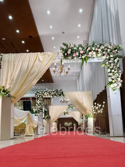 A grand entryway for a wedding reception, featuring multiple floral arches with chandeliers and a red carpet. This is how we make your guests feel special from the moment they arrive.
