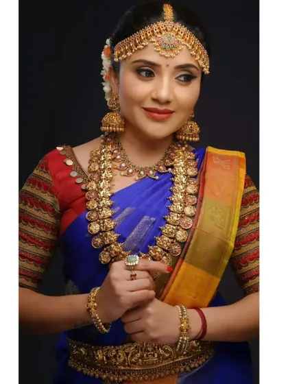 A gorgeous muhurtham look featuring a traditional kasu mala. The coin necklace is paired with a choker and jhumkas, creating a rich, layered effect that is perfect for a royal blue saree.