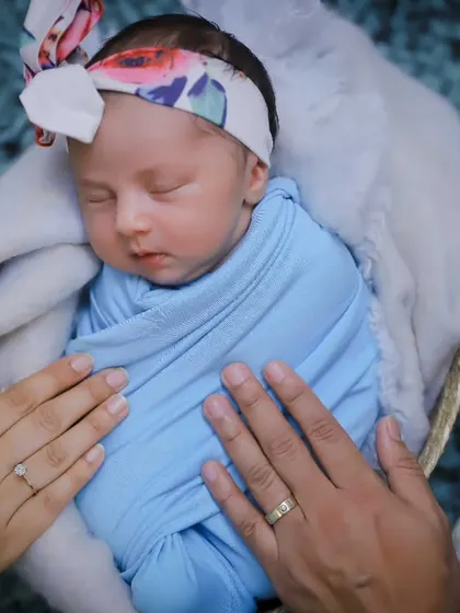 A peacefully sleeping newborn, swaddled in blue, with her parents' hands resting gently on her. A perfect studio newborn portrait.