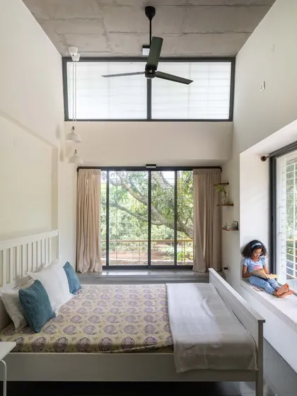 The bedroom at "Aamra" is a tranquil space with a high, sloping ceiling and clerestory windows. The built-in window seat provides a cozy corner to enjoy the view of the mango trees.