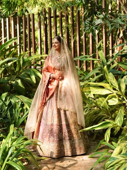 A wide shot showing the bride in a beautiful garden. Her pastel lehenga and glowing makeup make her look like she's stepped out of a fairytale.