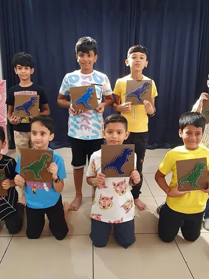 A group of boys proudly show off the dinosaur string art they made at a birthday party. Art is for everyone.