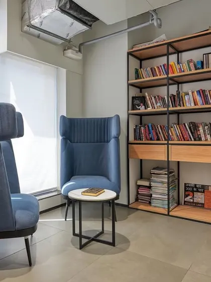 A quiet reading corner with high-backed blue armchairs that provide visual and acoustic privacy. A small bookshelf makes it a perfect spot to unwind.