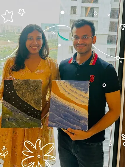 A couple proudly displays their finished textured art pieces. Each canvas tells a unique story through its colors and sculpted layers, one depicting a starry night and the other abstract ocean waves.
