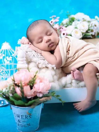 A profile shot of a newborn sleeping on a tiny bed prop. The composition with flowers in the foreground adds depth and visual interest to the photograph.