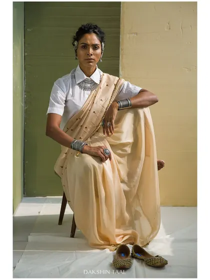 A seated portrait that exudes quiet confidence. The composition is strong and centered, showcasing the full look from the jewelry to the traditional footwear.