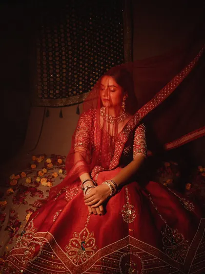 A classic bridal pose, with the veil gently covering the model. The deep red tones and soft lighting create a feeling of romance and tradition.
