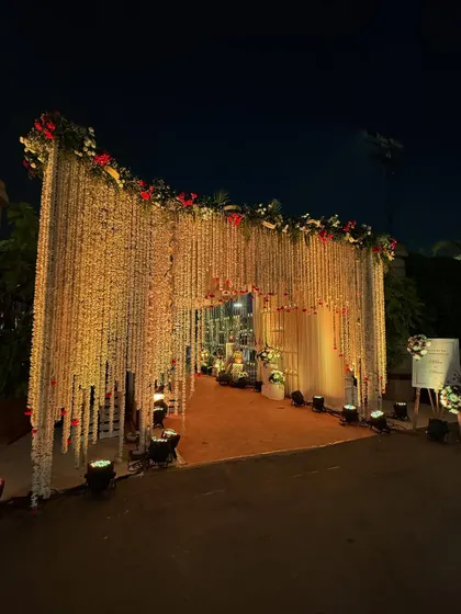 A grand entrance featuring a massive curtain of white floral strings, topped with red and white flowers. The scale of this installation creates a huge "wow" factor for guests upon arrival.