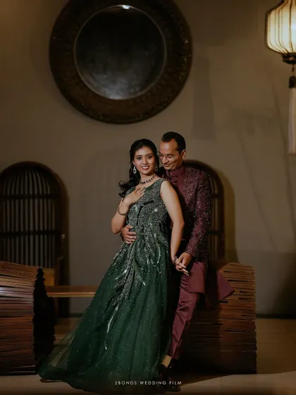 An elegant portrait of a couple in their reception attire, the bride in a stunning green gown and the groom in a complementary maroon sherwani.