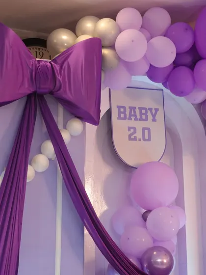 A close-up of the 'Baby 2.0' sign and the oversized purple bow, a playful nod to the family's second child.