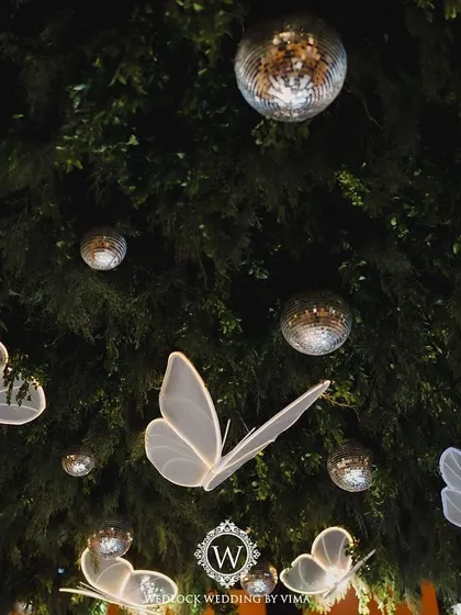 A walkthrough of a sangeet with an enchanted forest theme. The decor features a ceiling of lush greenery, sparkling disco balls, and glowing LED butterflies, creating a truly magical atmosphere.