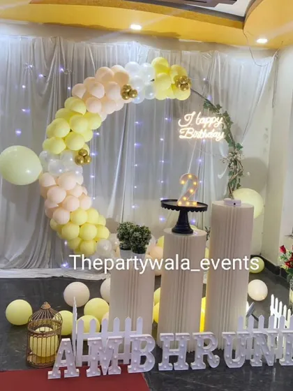 A pastel yellow and white balloon ring with a 'Happy Birthday' neon sign and fairy lights.